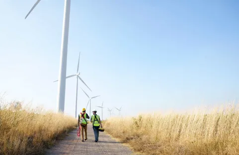 Due operai specializzati davanti a delle turbine eoliche onshore in un campo di grano