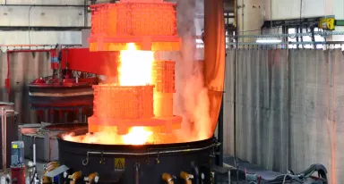 Paniers de pièces métalliques incandescentes et flammes au-dessus d'un bac de trempe.